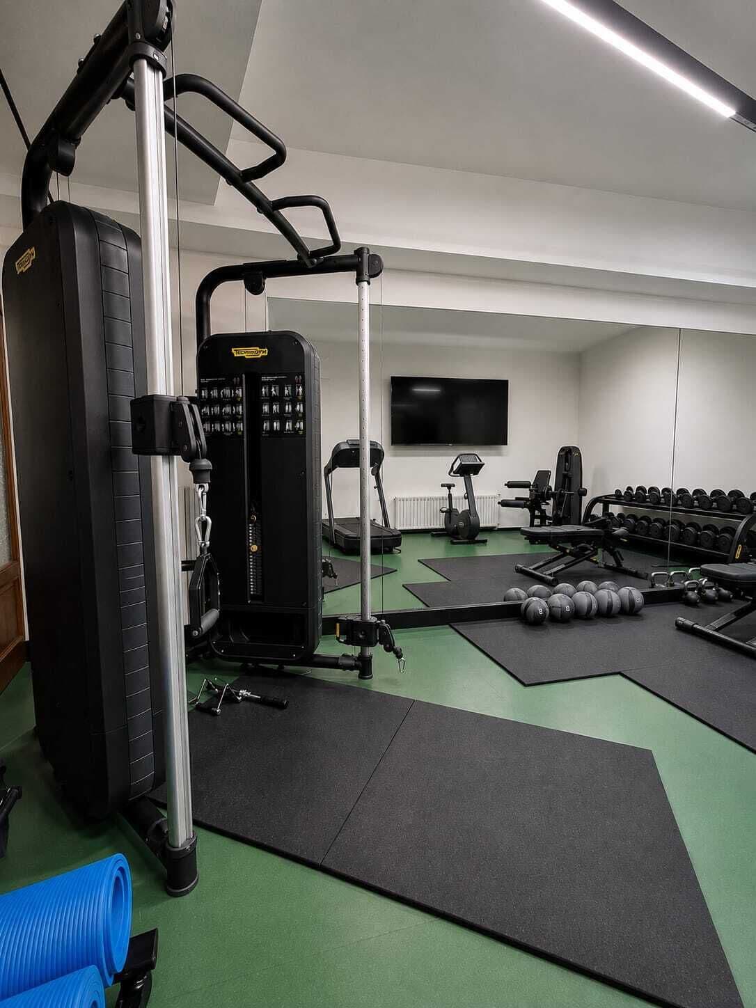 Un gimnasio con equipo de ejercicio, pesas y un televisor en la pared.