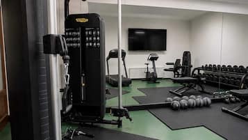 Un gimnasio con equipo de ejercicio, pesas y un televisor en la pared.
