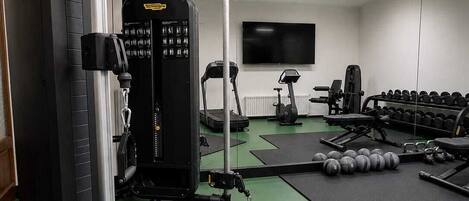 Un gimnasio con equipo de ejercicio, pesas y un televisor en la pared.
