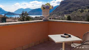 A balcony with a table, chairs, a vase of flowers, and a view of mountains and a lake.