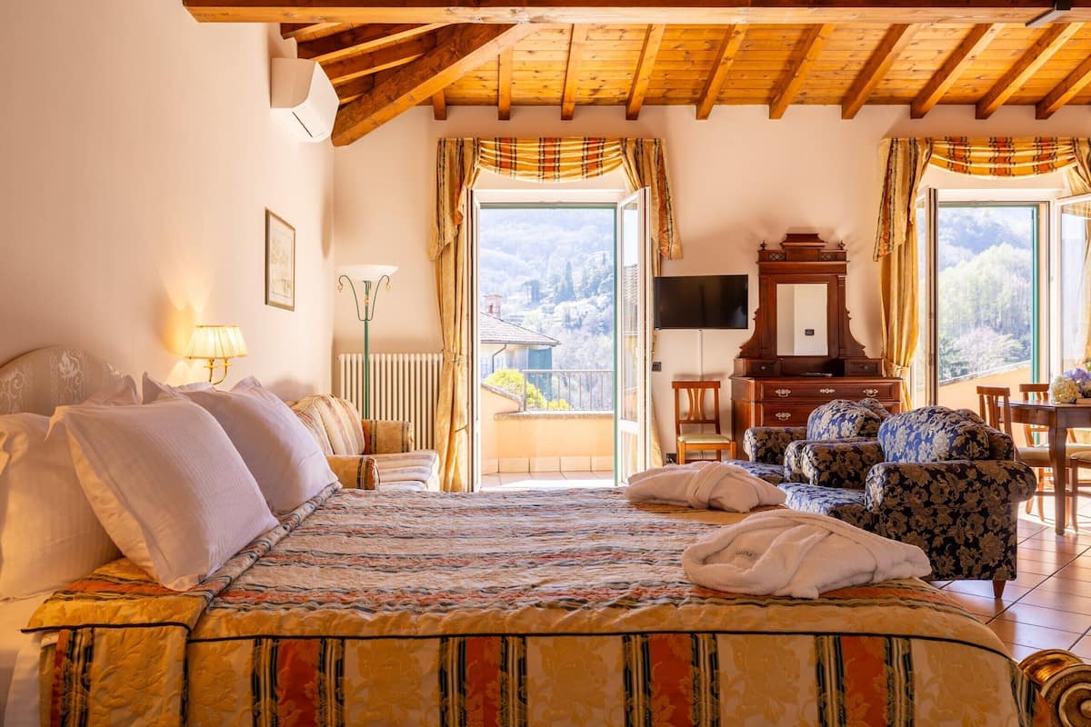 A bedroom with a bed, a TV, a wooden ceiling, a window with curtains, and a view of the outside.