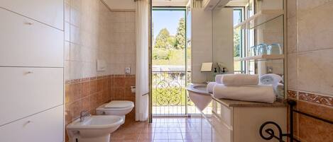 A bathroom with a toilet, bidet, and sink, a balcony with a view, and a tiled floor.