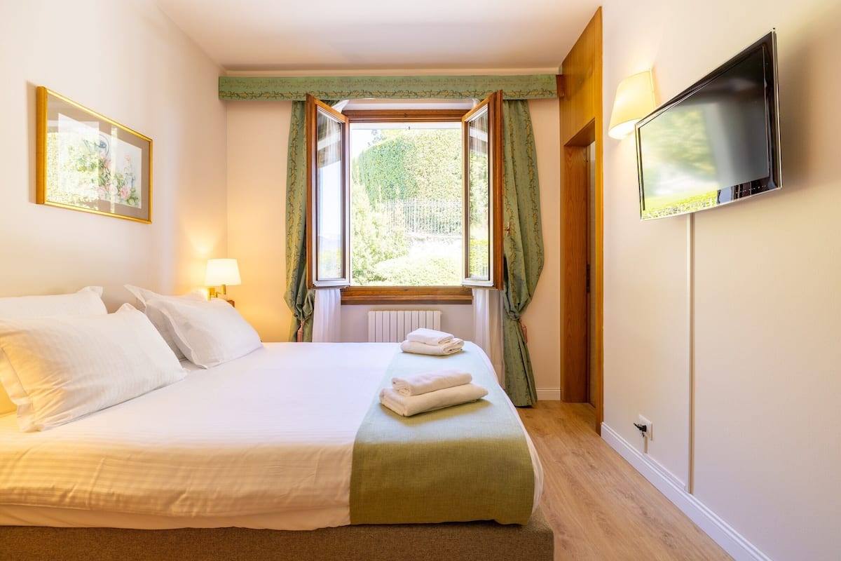 A hotel room with a bed, a television, a window with curtains, and a framed picture on the wall.