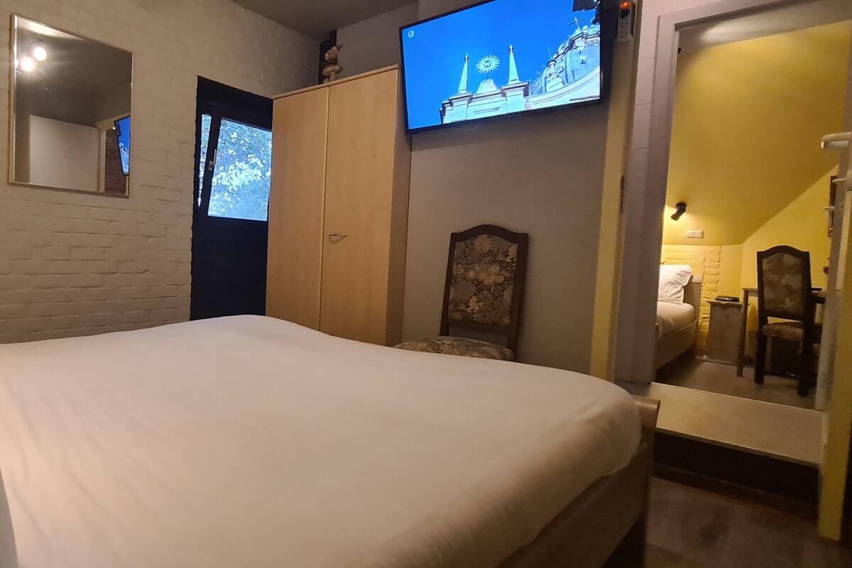 Een slaapkamer met een bed, een aan de muur bevestigde televisie, een kledingkast en een spiegel.