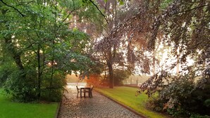 A cobblestone pathway in a park with a bench and trees. - Hotel Landhuis ' T Wilgenerf (Ypres)