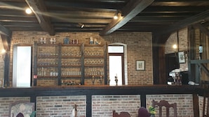 A rustic bar area with wooden shelves displaying glassware and bottles, a brick wall, and a wooden ceiling. - Hotel Landhuis ' T Wilgenerf (Ypres)