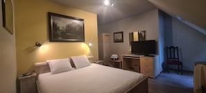 A hotel room with a bed, bedside tables, a desk with a chair, a television, and framed pictures on the walls.