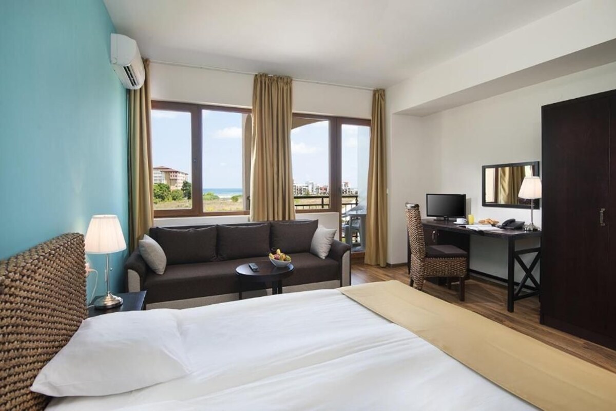 A hotel room with a bed, a sofa, a desk, a TV, and a view of the outdoors.