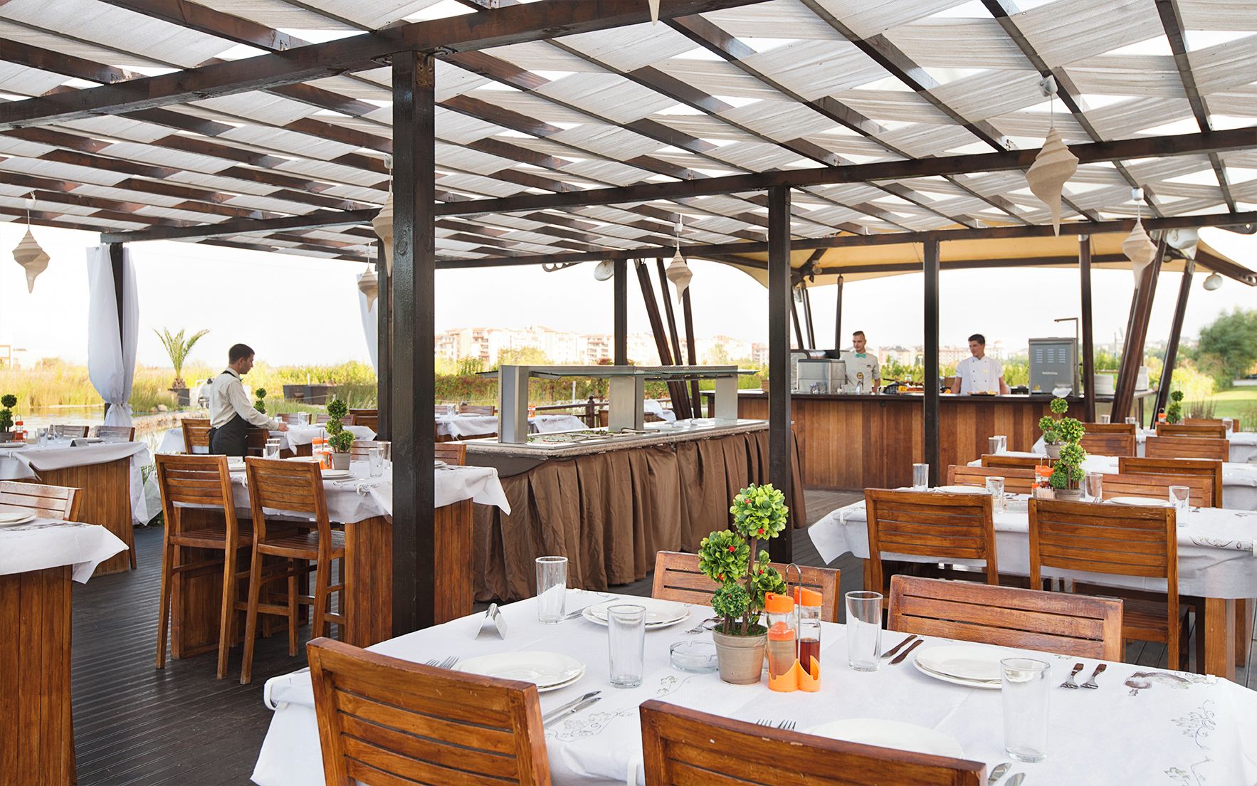 Un restaurante al aire libre con mesas y sillas de madera, una zona de bar y vistas del paisaje circundante.