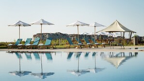 A poolside area with lounge chairs and umbrellas, reflecting the pool and surrounding buildings. - Sunrise All Suites Resort (Nessebar)