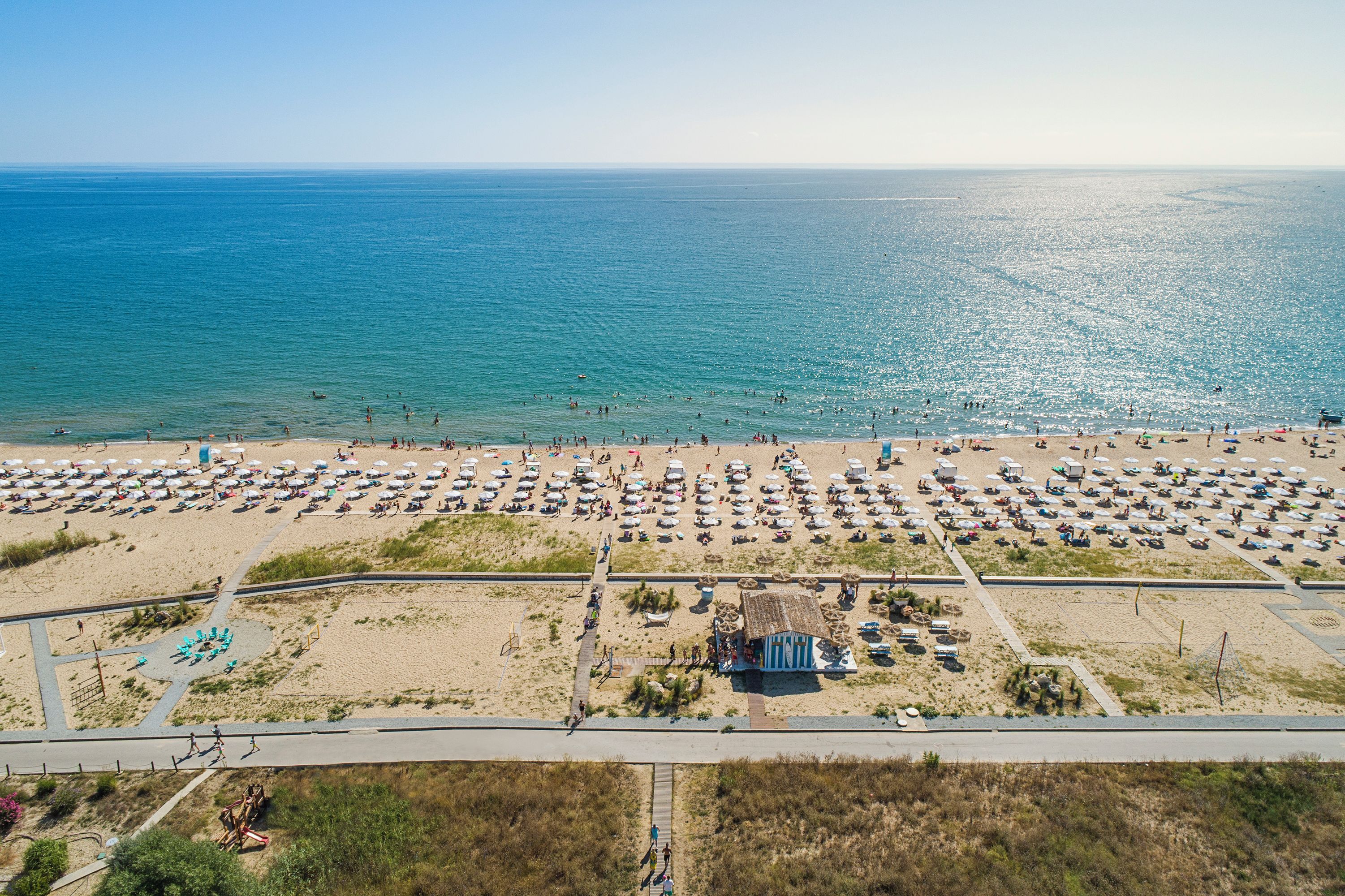 Vista aérea de una playa con numerosas tumbonas y sombrillas, una pequeña cabaña y una carretera que discurre paralela a la playa.