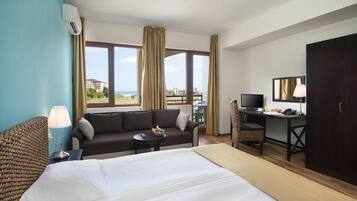 Habitación de hotel con cama, sofá, escritorio, televisor y vista al exterior.