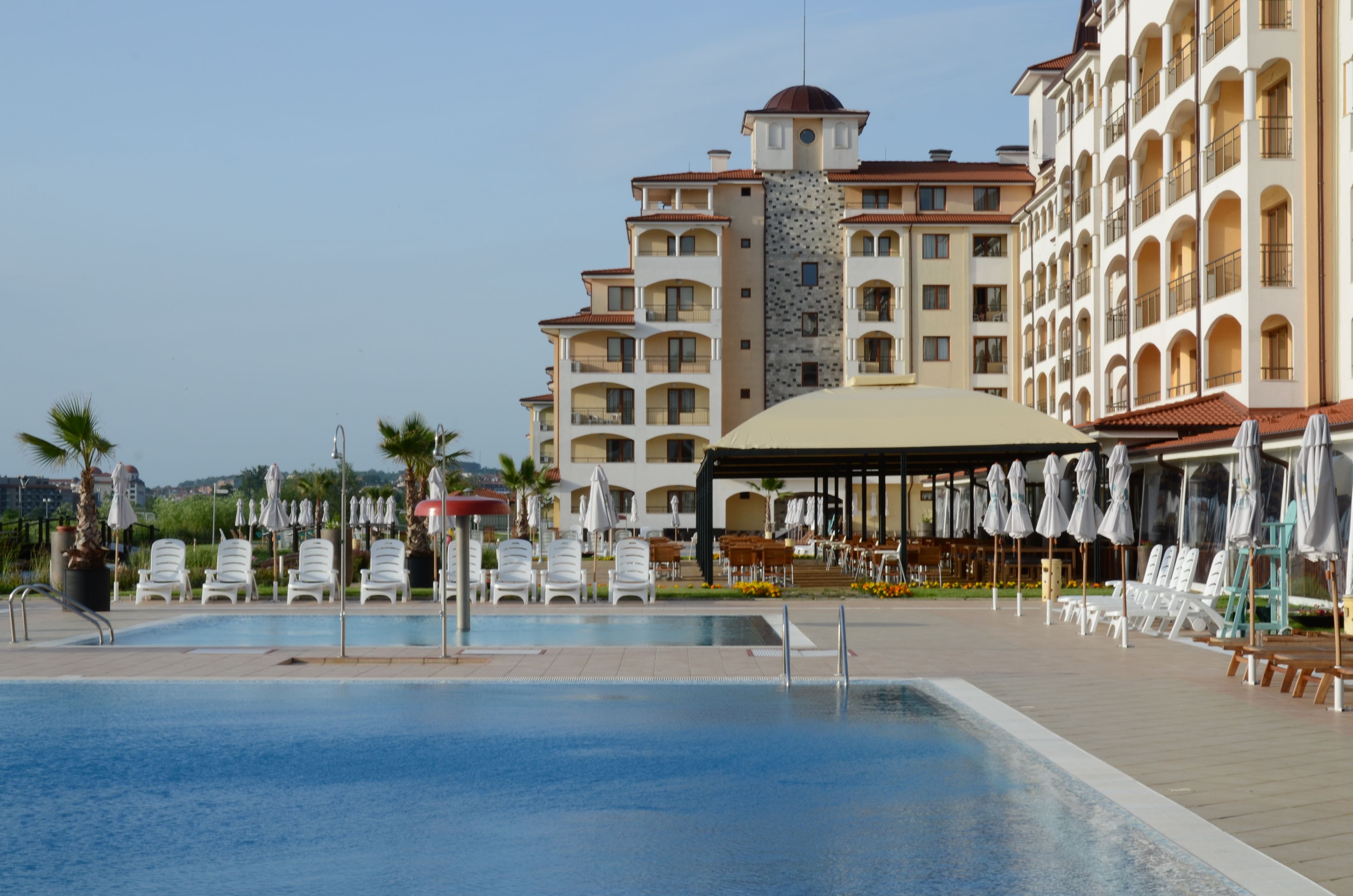 Un hotel con piscina, mesas al aire libre y una zona cubierta con sombrillas.