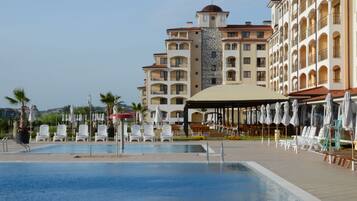 Un hotel con piscina, mesas al aire libre y una zona cubierta con sombrillas.