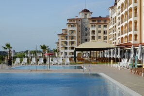 Un hotel con piscina, mesas al aire libre y una zona cubierta con sombrillas.
