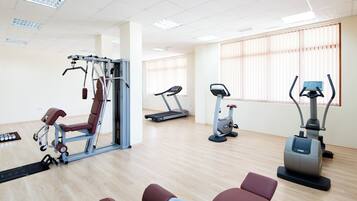 Un gimnasio con máquinas de cardio, equipo de entrenamiento de fuerza y una pared de espejos.