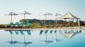 Ein Poolbereich mit Liegestühlen und Sonnenschirmen, dessen Spiegelung sich im Wasser zeigt.