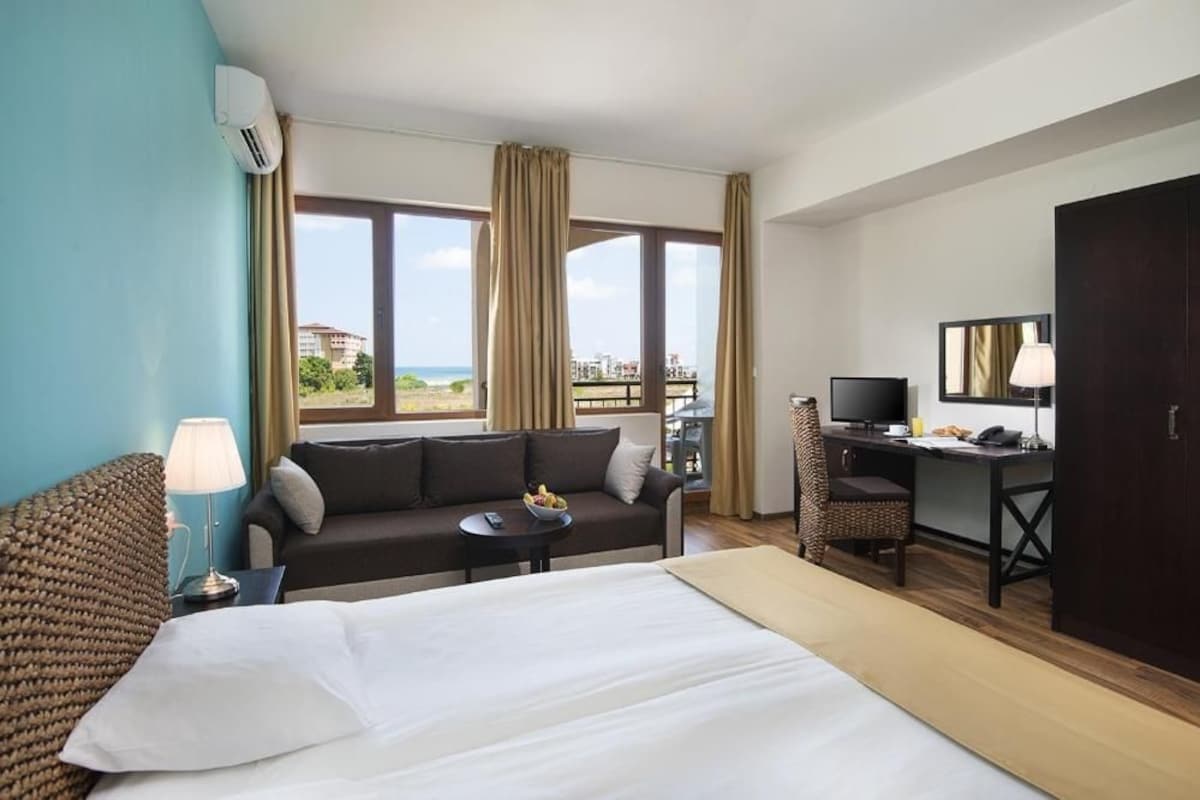 A hotel room with a bed, a sofa, a desk, a TV, and a view of the outdoors.