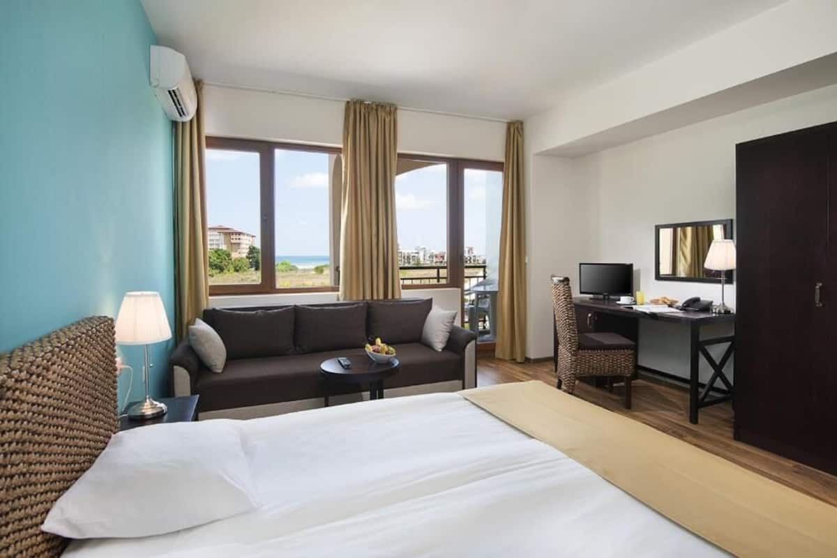 A hotel room with a bed, a sofa, a desk, a TV, and a view of the outdoors.