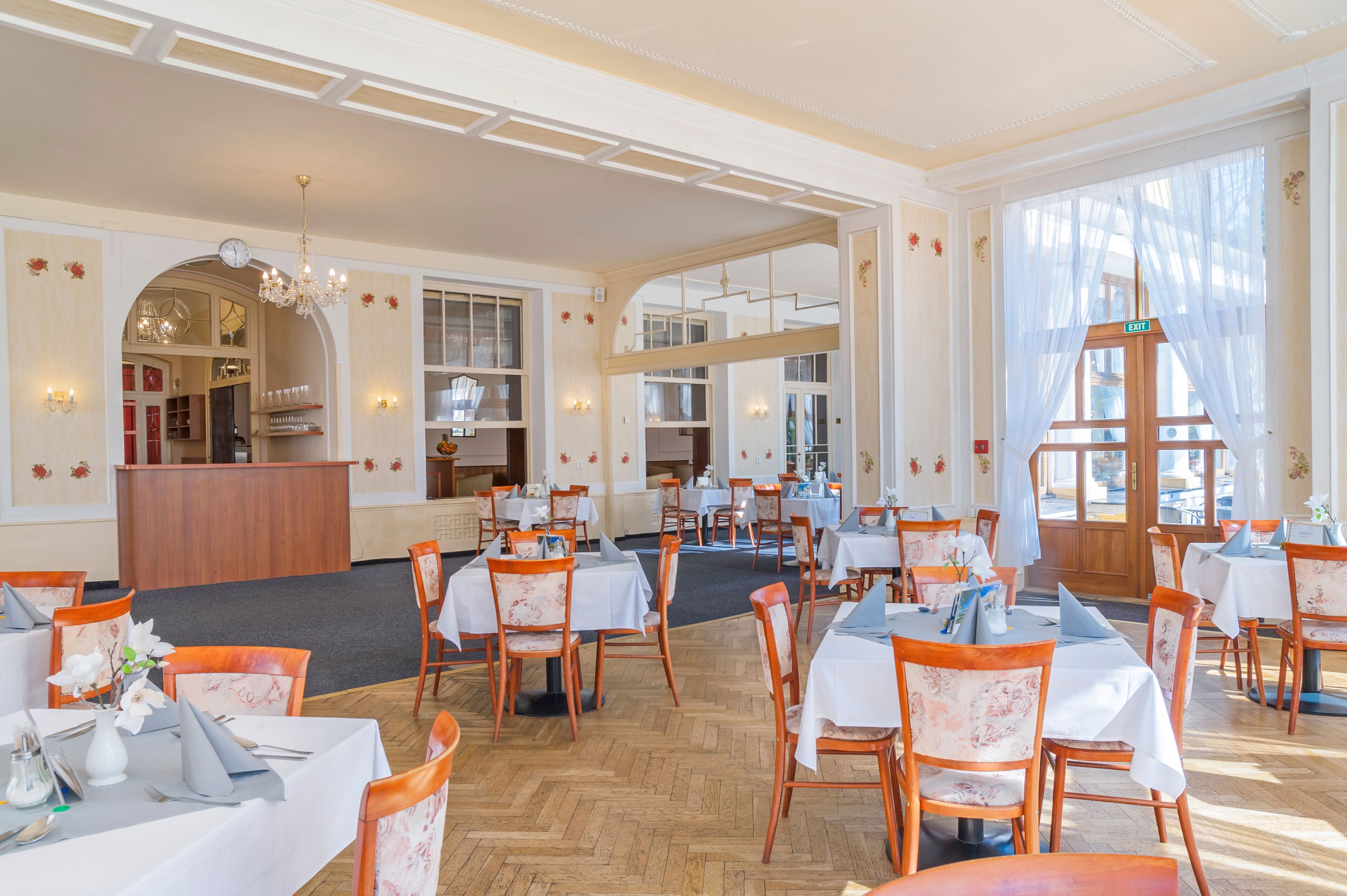 A spacious dining area with multiple tables and chairs, a reception desk, and large windows allowing natural light.