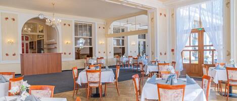 A spacious dining area with multiple tables and chairs, a reception desk, and large windows allowing natural light.
