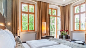 Une chambre d’hôtel avec un grand lit, un bureau et une vue sur la verdure par les fenêtres.