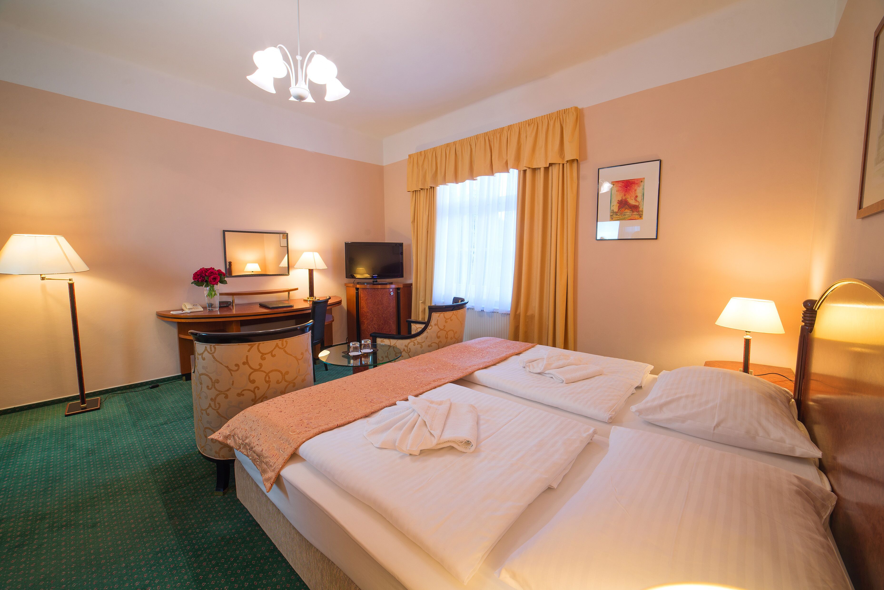 A hotel room with a bed, two bedside tables, a desk with a chair, a television, and a window with curtains.
