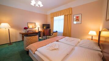 A hotel room with a bed, two bedside tables, a desk with a chair, a television, and a window with curtains.