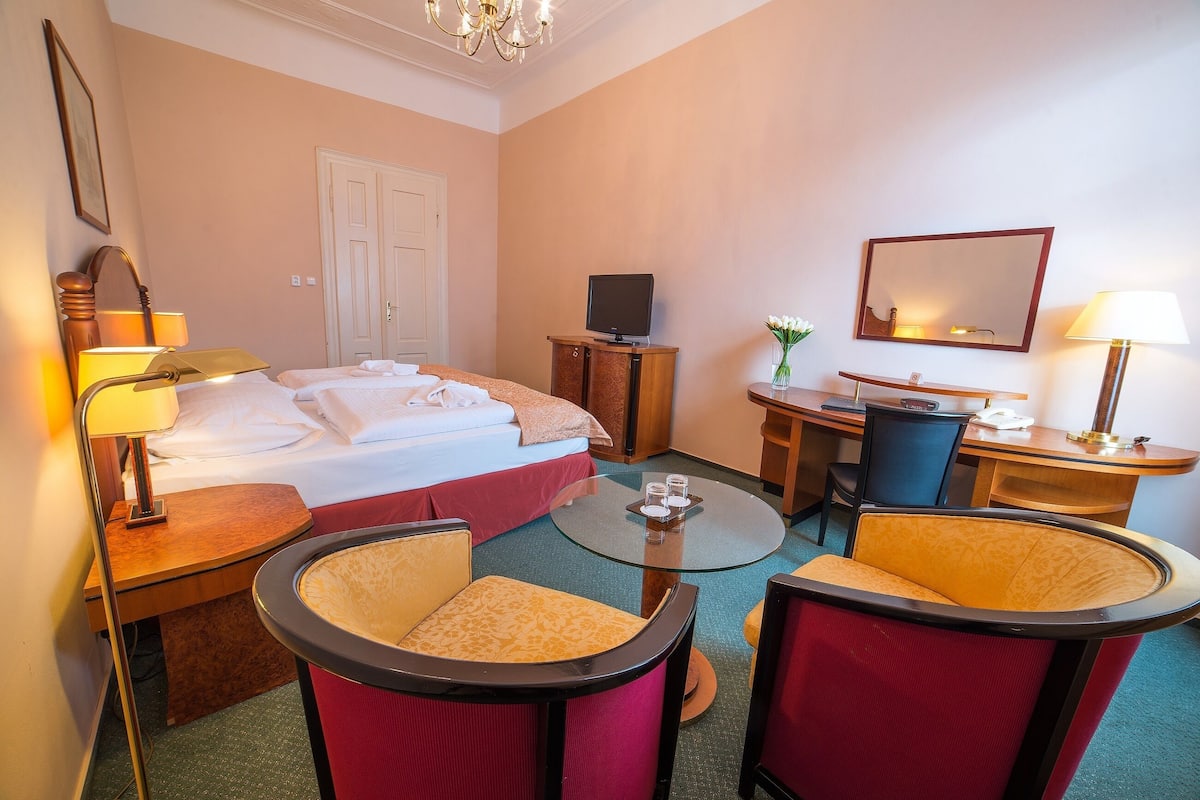 Ein Hotelzimmer mit Bett, Schreibtisch, zwei Stühlen, Fernseher und Spiegel.