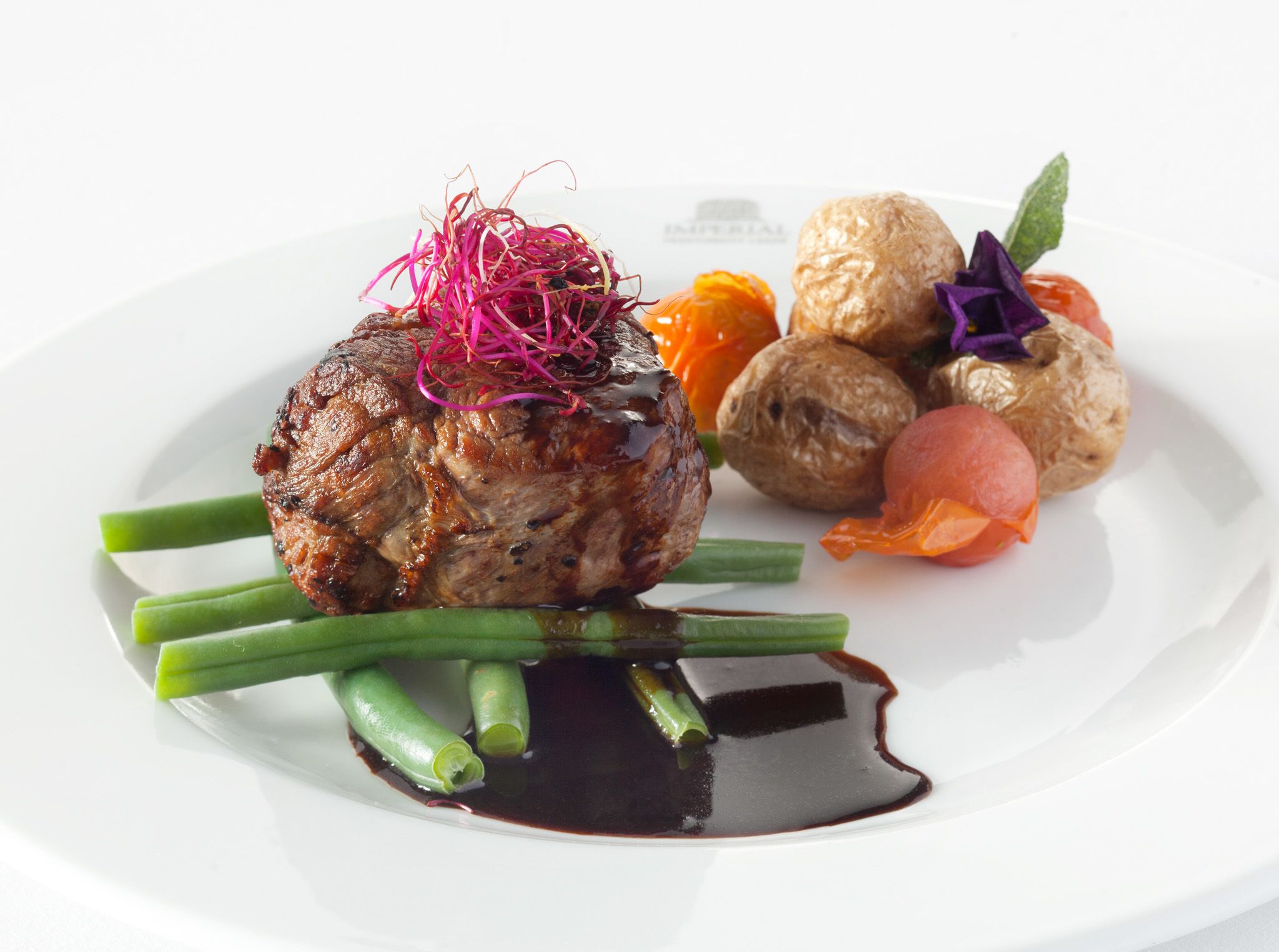 Un plato con filete, espárragos verdes y salsa oscura.