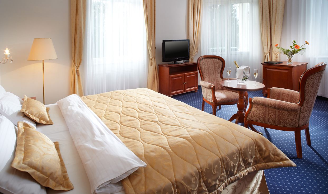 Une chambre d’hôtel avec un grand lit, une télévision, un bureau avec une chaise et une petite table sur laquelle est posé un vase de fleurs.