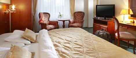 A hotel room with a large bed, two armchairs, a television, a desk with a lamp, and a minibar.