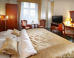 Una habitación de hotel con una cama grande, dos sillones, un televisor, un escritorio con lámpara y un minibar.