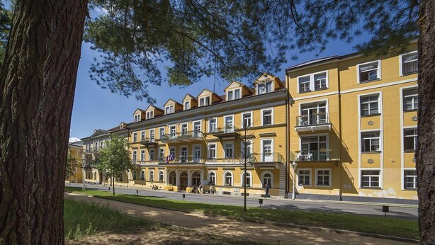 Una hilera de edificios amarillos de varios pisos con balcones, un sendero pavimentado y un árbol en primer plano.