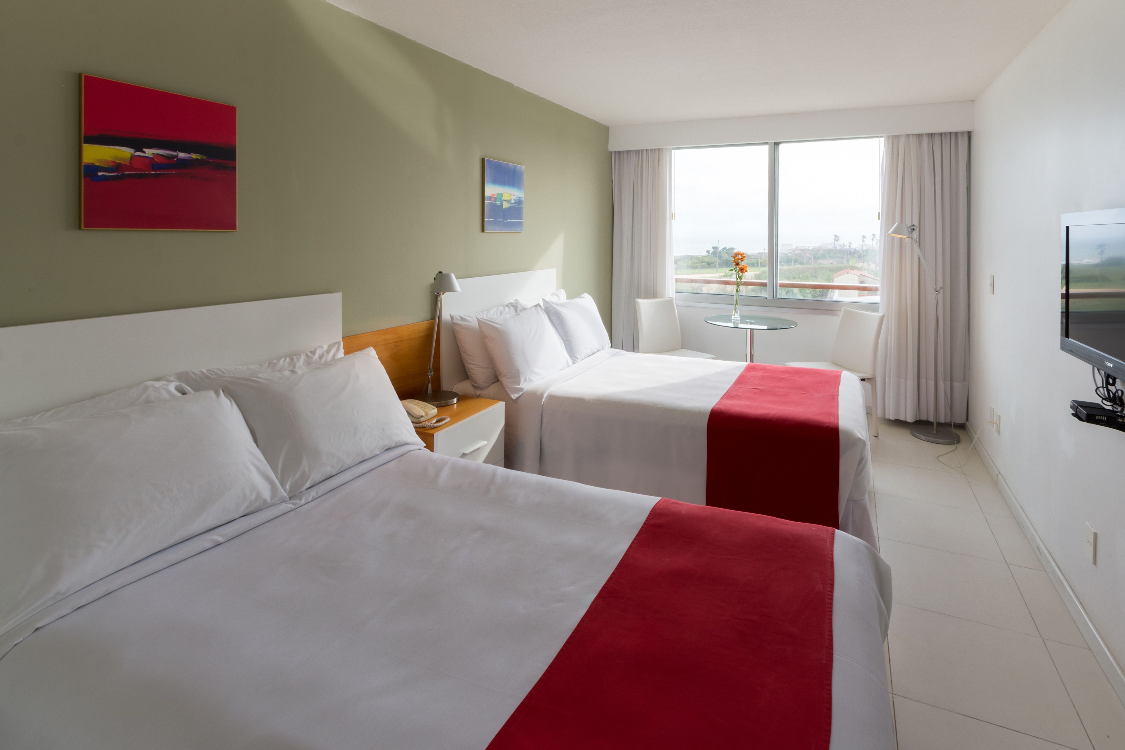 Habitación de hotel con dos camas, televisión, una mesita con una silla y ventana con vistas.