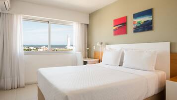 Habitación de hotel con una cama grande, un escritorio, una silla y vistas al mar y un faro.