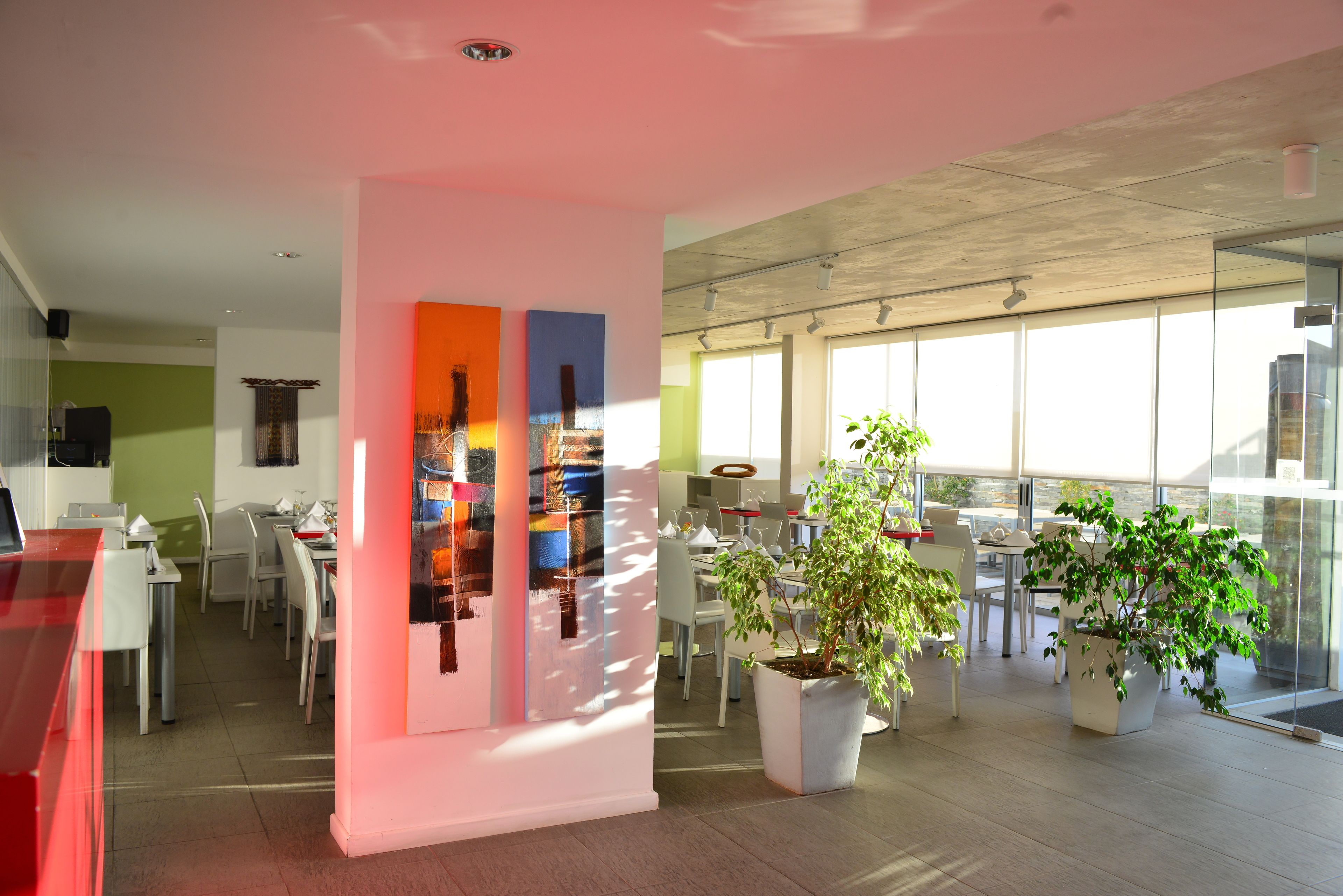 A modern dining area with a glass partition, a red counter, and potted plants.