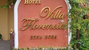 A sign for Hotel Villa Florencia Zona Rosa with a decorative arch and greenery.