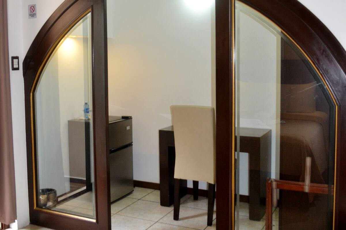 A hotel room with a bed, a desk, a chair, and a television mounted on the wall.