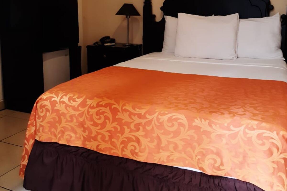 A hotel room with a large bed, a nightstand, a lamp, and a wardrobe.
