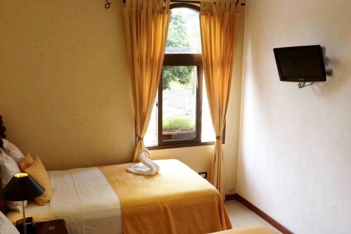 A hotel room with two beds, a television on the wall, and a window with curtains.
