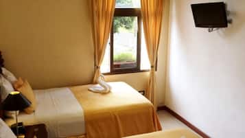 A hotel room with two beds, a television on the wall, and a window with curtains.