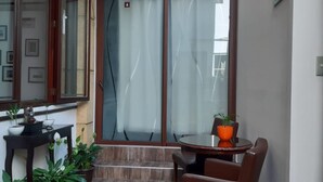 A small balcony with a round table and two chairs, potted plants, and a sliding glass door.