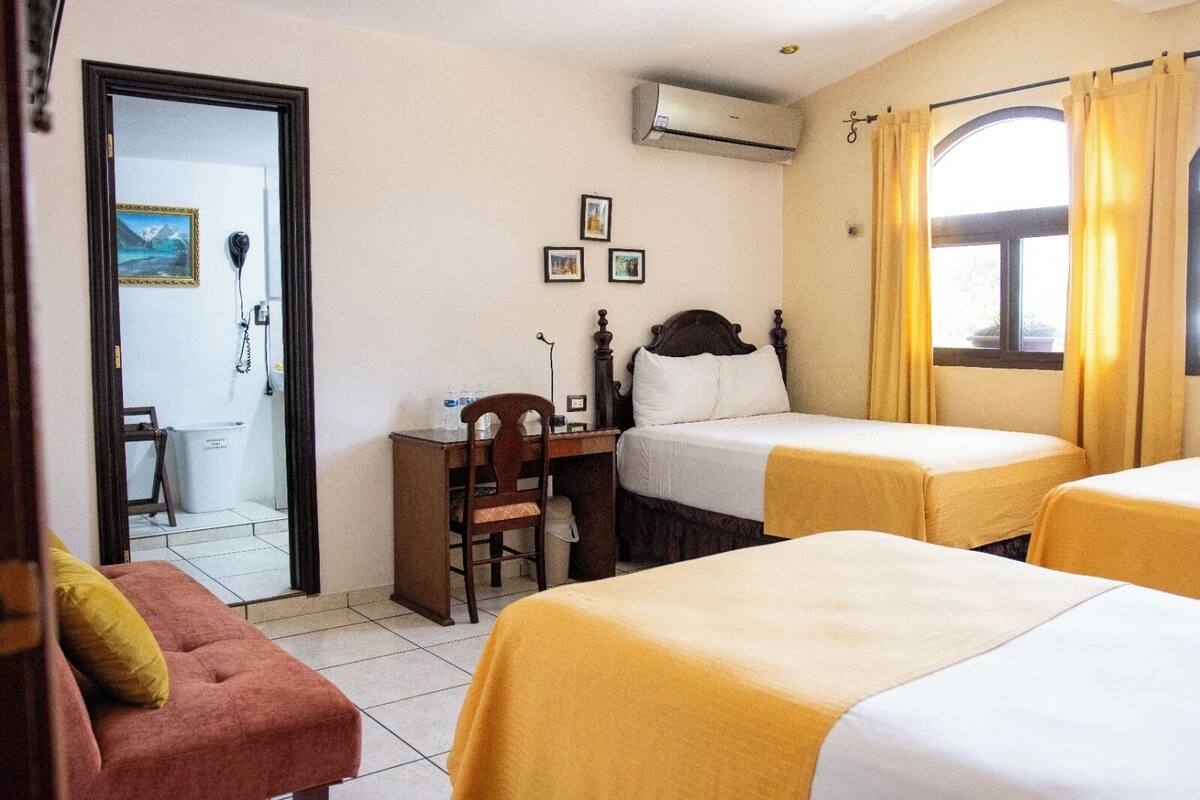 A hotel room with two beds, a desk, a chair, and an air conditioning unit.