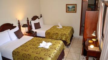 A hotel room with two beds, each with floral bedspreads, a painting on the wall, and a desk with a lamp.