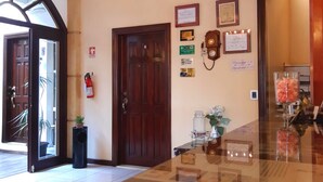 A lobby with a wooden door, a fire extinguisher, and several framed certificates on the wall.