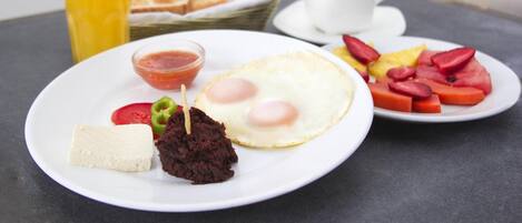 A breakfast plate with eggs, tomatoes, and a small bowl of sauce, a glass of orange juice, and a cup of coffee on a table.