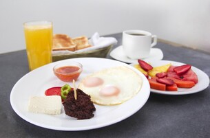 A breakfast plate with eggs, tomatoes, and a small bowl of sauce, a glass of orange juice, and a cup of coffee on a table.