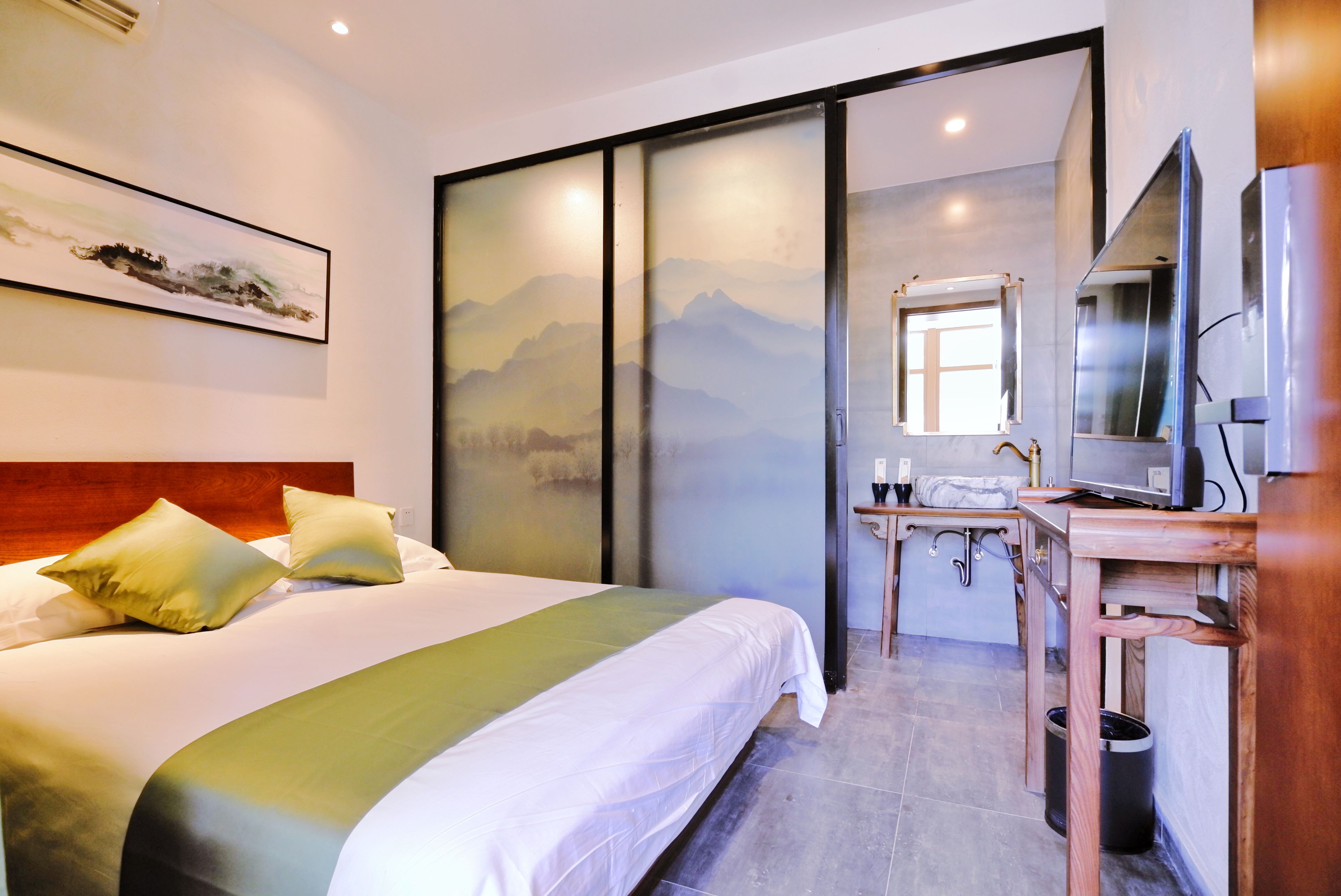 A hotel room with a bed, a desk, a mirror, and a TV.
