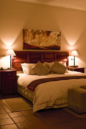 A neatly made bed with a wooden headboard, two bedside tables with lamps, and a painting above the bed. - Tzaneen Country Lodge (Tzaneen)